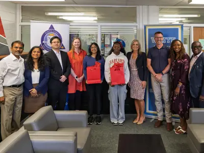 a group photo of school officials with two teenage girls in the middle holding red gift bags. 
