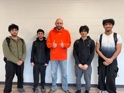 four students posing with a teacher in a school hallway. 