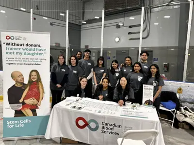 a group of students posing behind a blood donation campaign table. 