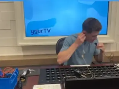 a boy sitting in front of a screen working on a machine while wearing headphones. 