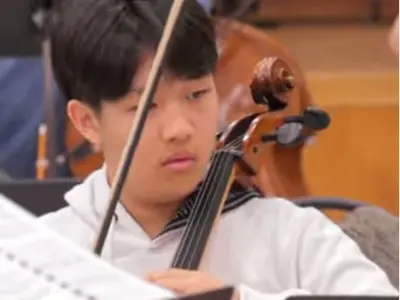 close up of a teenage boys face while playing the cello. 
