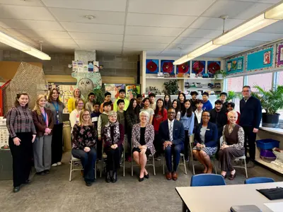 a large amount of people posing for a group photo in a school classroom