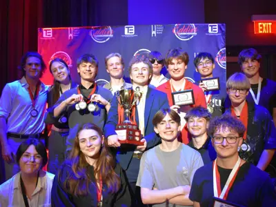 a group of teenagers posing for a picture on stage with the person in the middle holding up the trophy.