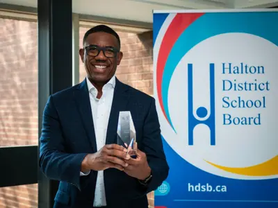 a close up of a man holding up an award in front of a Halton District School Board sign