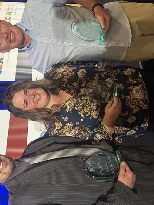 three adults posing side by side holding up glass awards